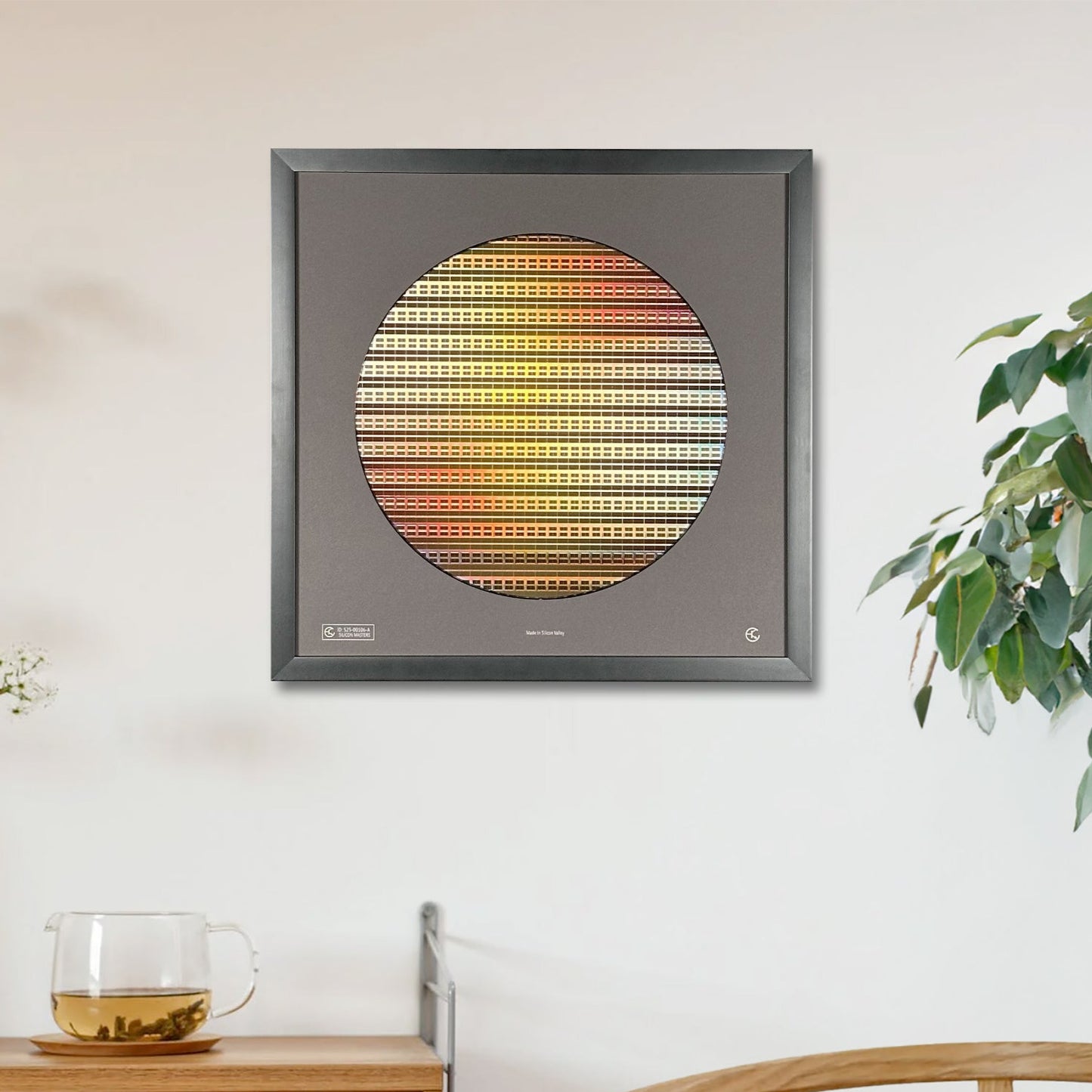 Framed circular artwork with a gradient pattern on a wall above a wooden side table with a plant and glass.