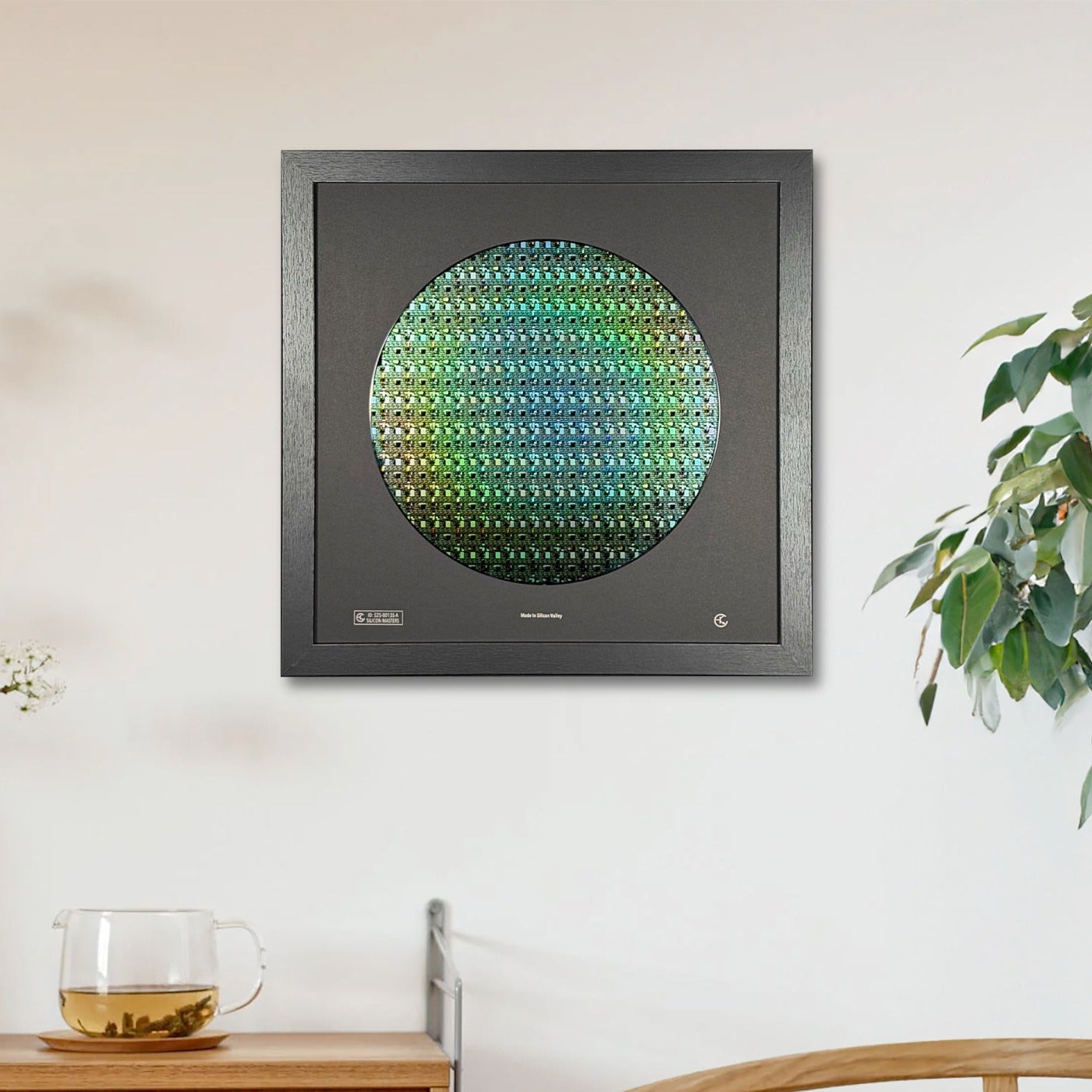 Framed artwork on a wall above a wooden cabinet with a plant and glass in the foreground.